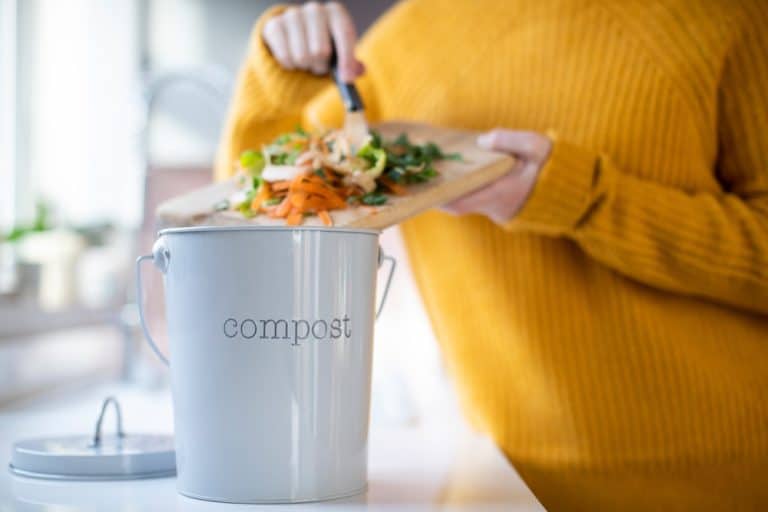 Close up of woman, yellow sweater, cooking ladling compost into countertop pail. La Jolla Composting