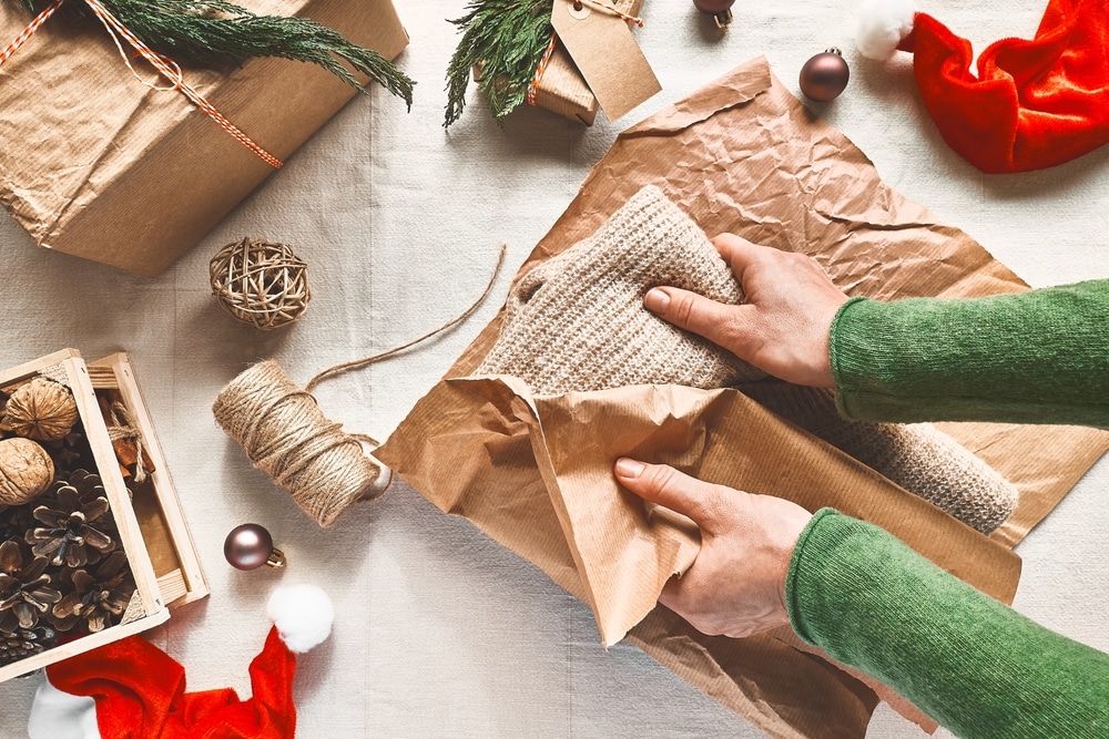 Two hands wrapping holiday gift, brown paper, twine, recycled materials, upcycling