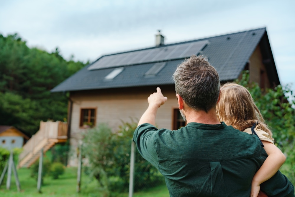 Man and young daughter pointing at a house with solar panels and vegetable plantings, green interior design, conscious design