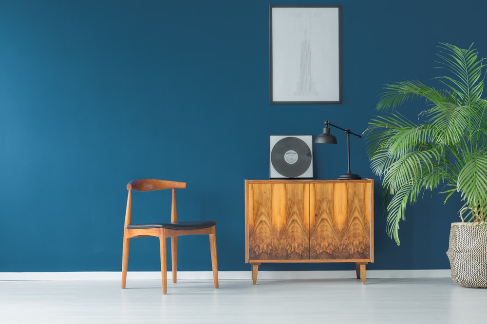 Mid century modern wooden chair and cabinet, reclaimed wood, dark blue walls, lamp and houseplant