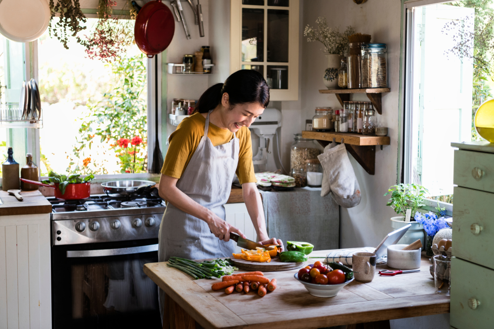 Asian woman preparing food in small Vegan kitchen, with window, cabinets, kitchen table