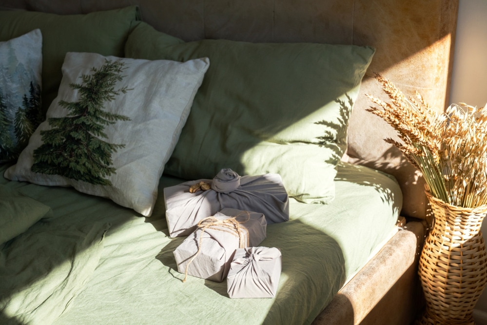 Cozy winter holiday interior with fabric wrapped presents on green couch and grain sheaf in baskets