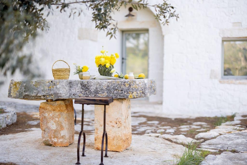 Stone table with flowerpot and basket in rustic Mediterranean courtyard of white-washed house